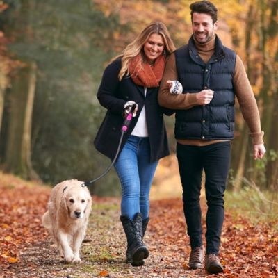 Homme avec sa femme dans le bois avec leur chien attaché à une laisse rétractable de couleur rose en toute sécurité